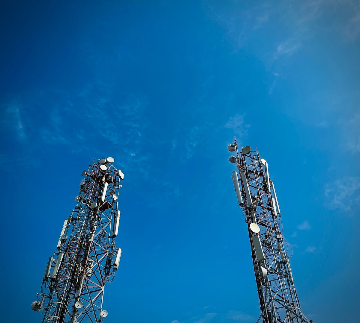 Two loaded telecom lattice towers against a deep blue sky
